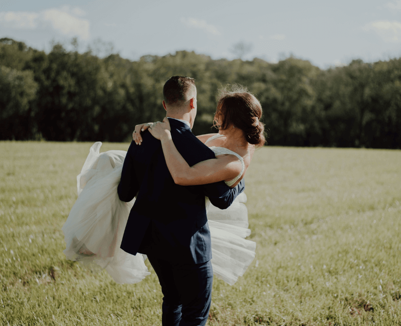 A groom carrying his bride through a field